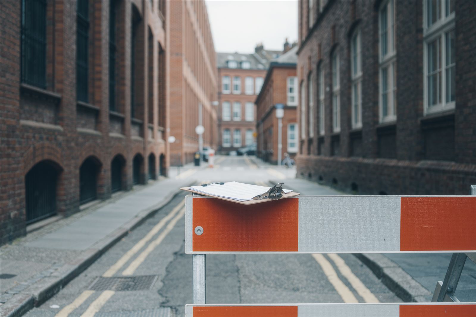 Orange and white traffic barricades across a closed brick-lined street with a clipboard of papers resting on the rail